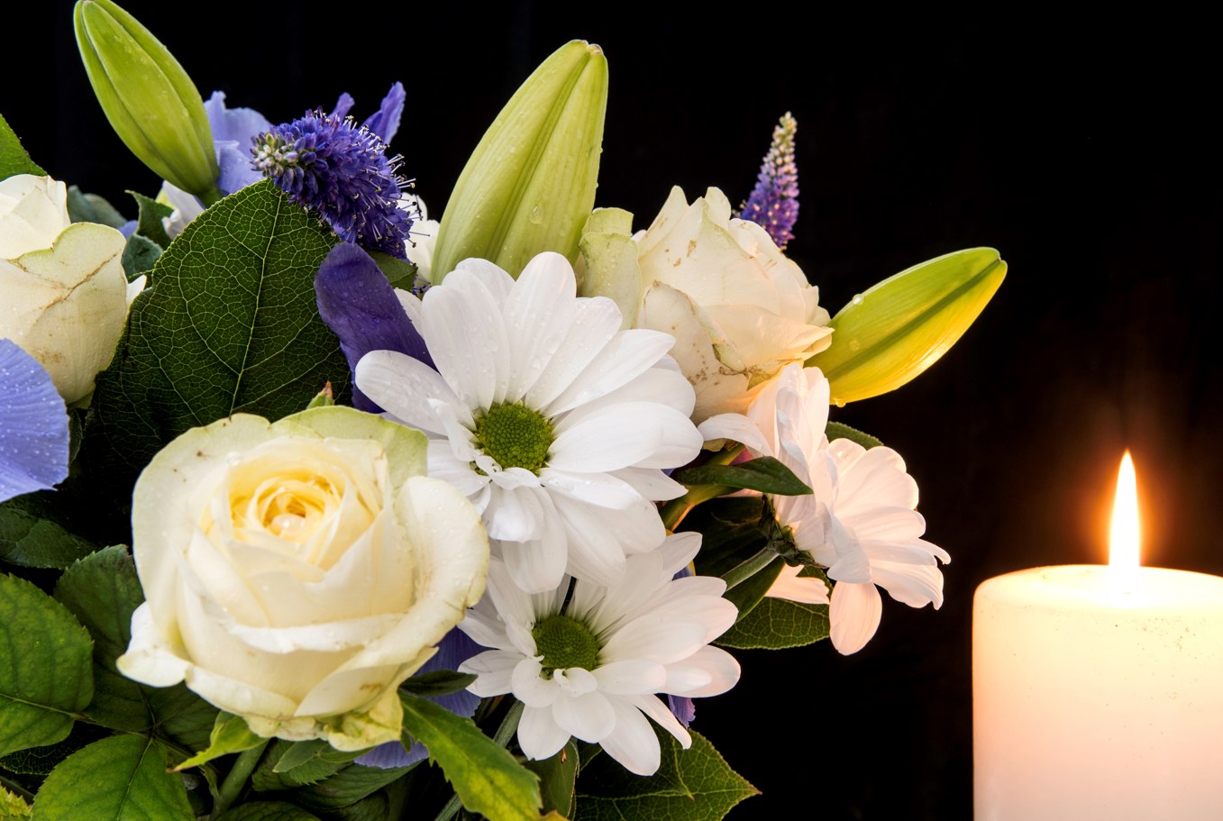 Bouquet de roses blanches, marguerites et fleurs mauves près d’une bougie allumée, sur fond noir